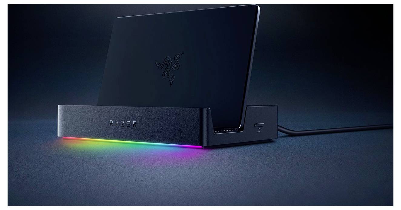 Laptop leží na elegantnom čiernom stojane so žiariacim RGB svetlom pod ním, čím zvyšuje moderný estetický dojem zostavy.