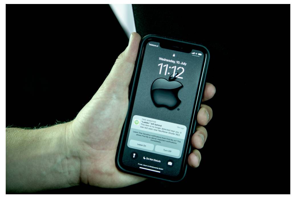 Ruka drží smartfón so zamykacou obrazovkou, na ktorej je veľké logo Apple, čas '11:12' a oznámenia.