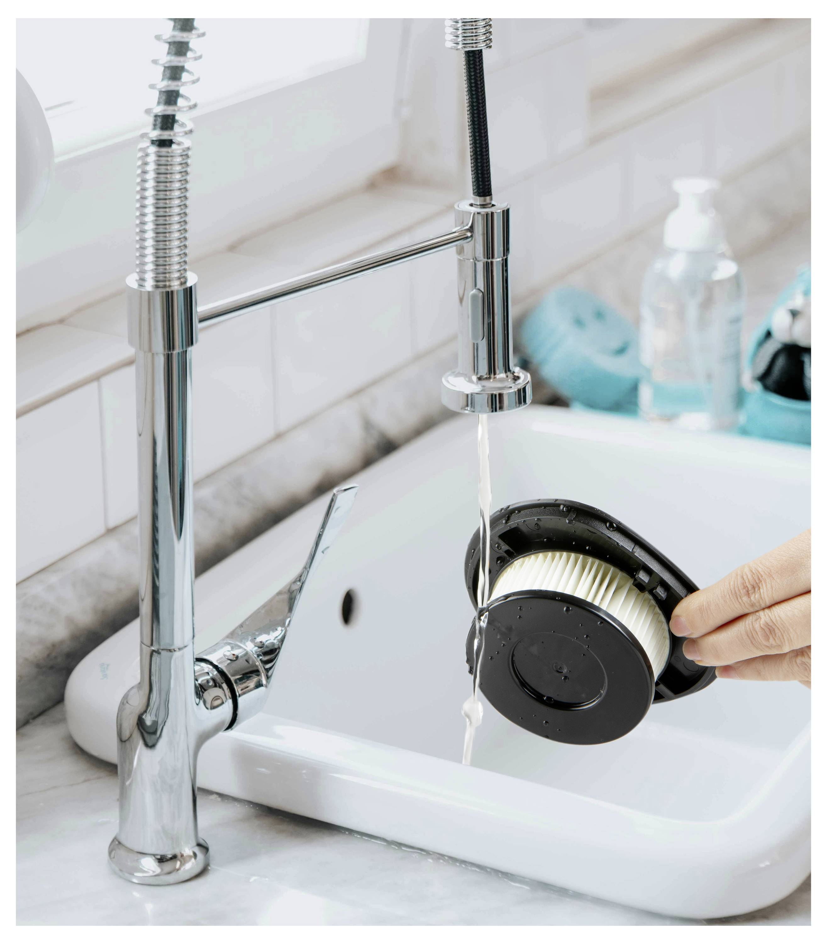 Osoba oplachuje filter vysávača pod kuchynskou vodovodnou batériou, pričom v pozadí sú viditeľné čistiace prostriedky.