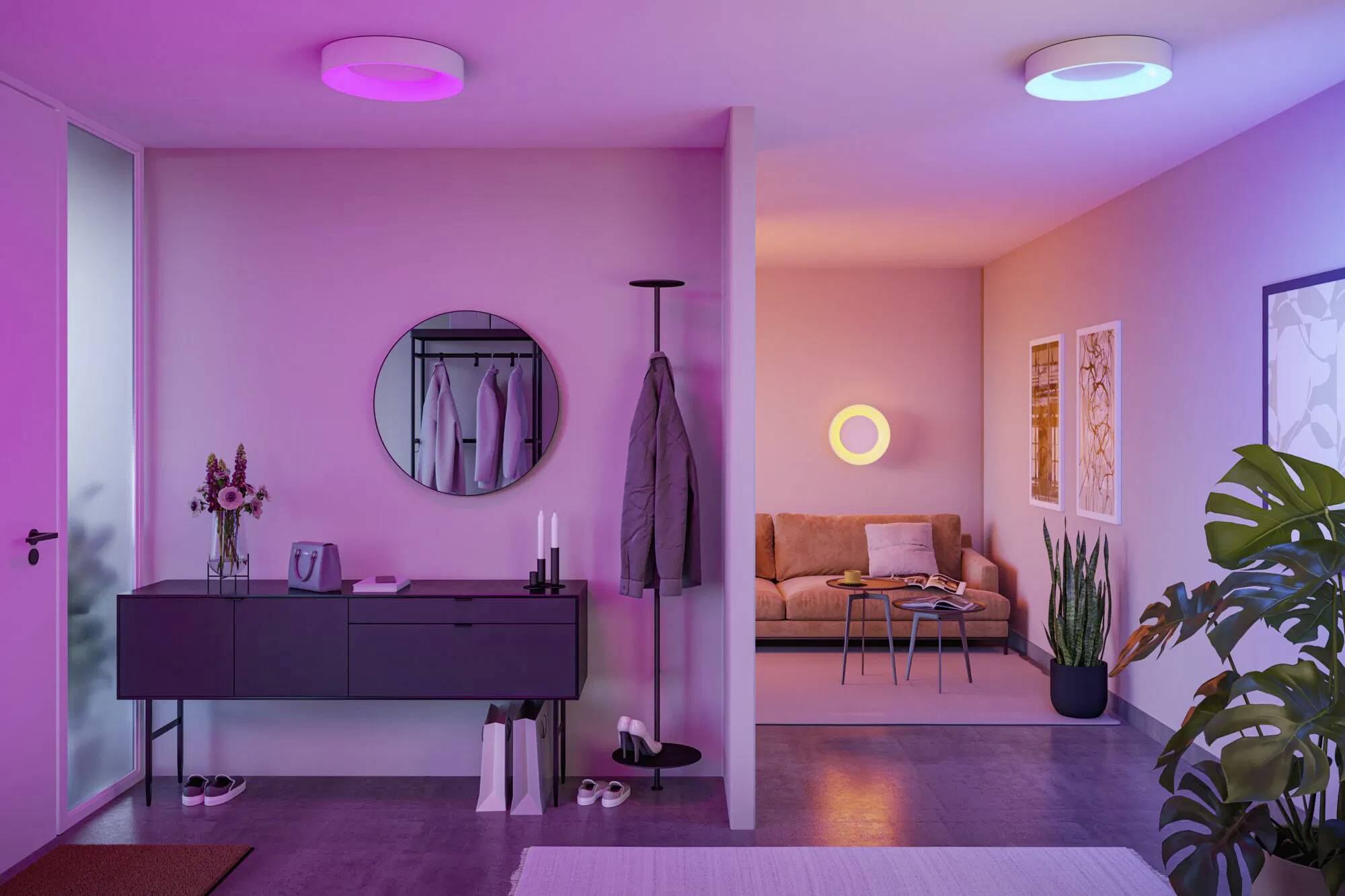 Moderná obývačka a chodba so farebnými stropnými svetlami, okrúhlym zrkadlom, vešiakom na kabáty a sedačkou. Dekorácie zahŕňajú rastliny a zarámované umelecké diela.