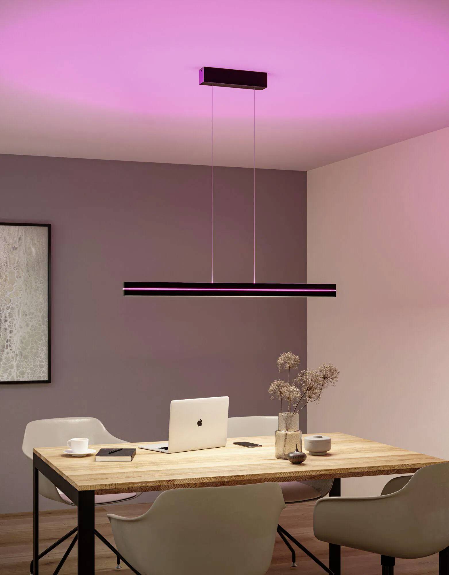 Moderná jedáleň so dreveným stolom, štyrmi stoličkami, laptopom a ružovo osvetleným stropom. Minimalistická výzdoba s visiacou svetelnou armatúrou.