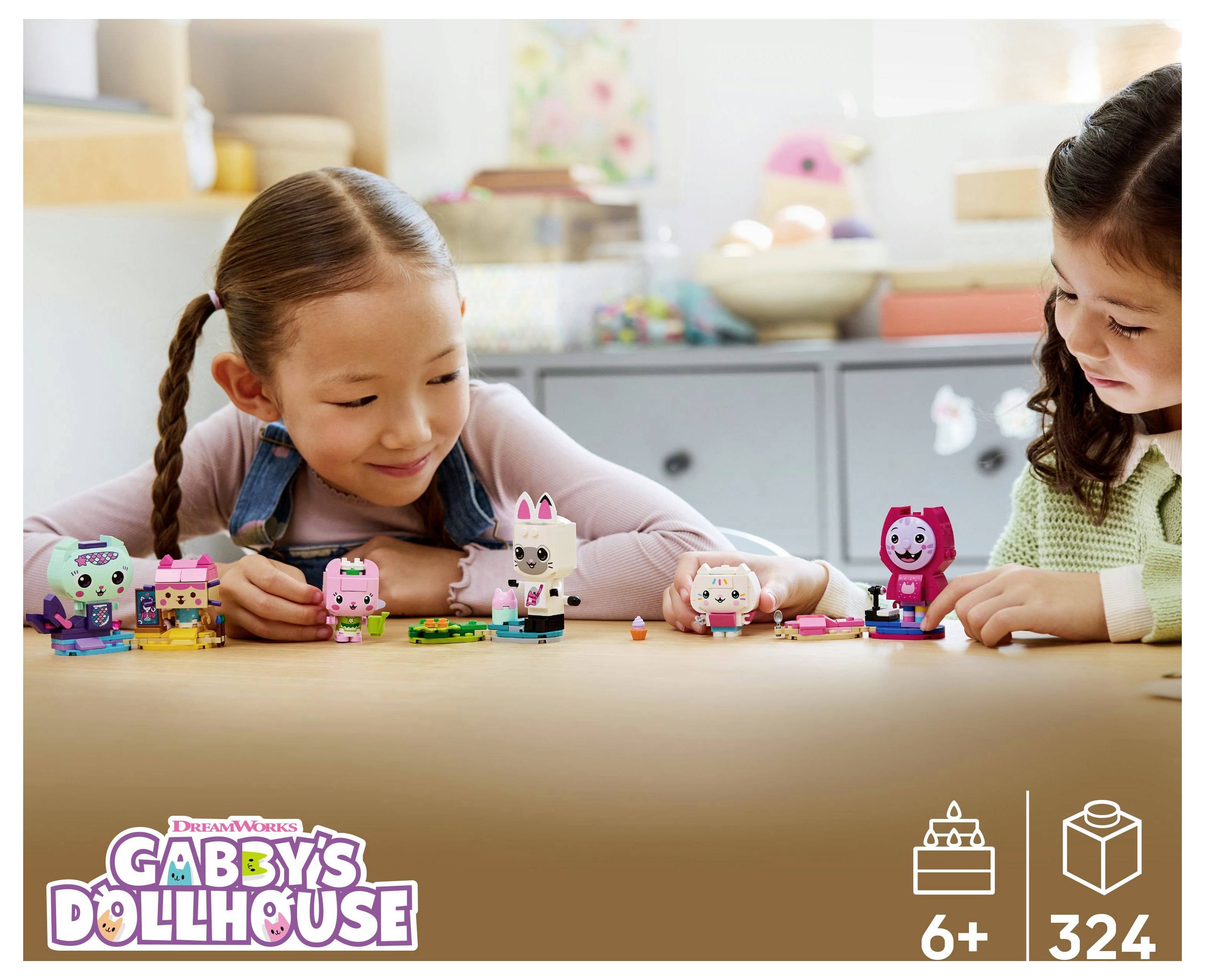 Dve deti sa hrajú s farebnými figúrkami z hračky 'Gabby's Dollhouse' na stole. Ikony na obale označujú vek 6+ a 324 kusov.