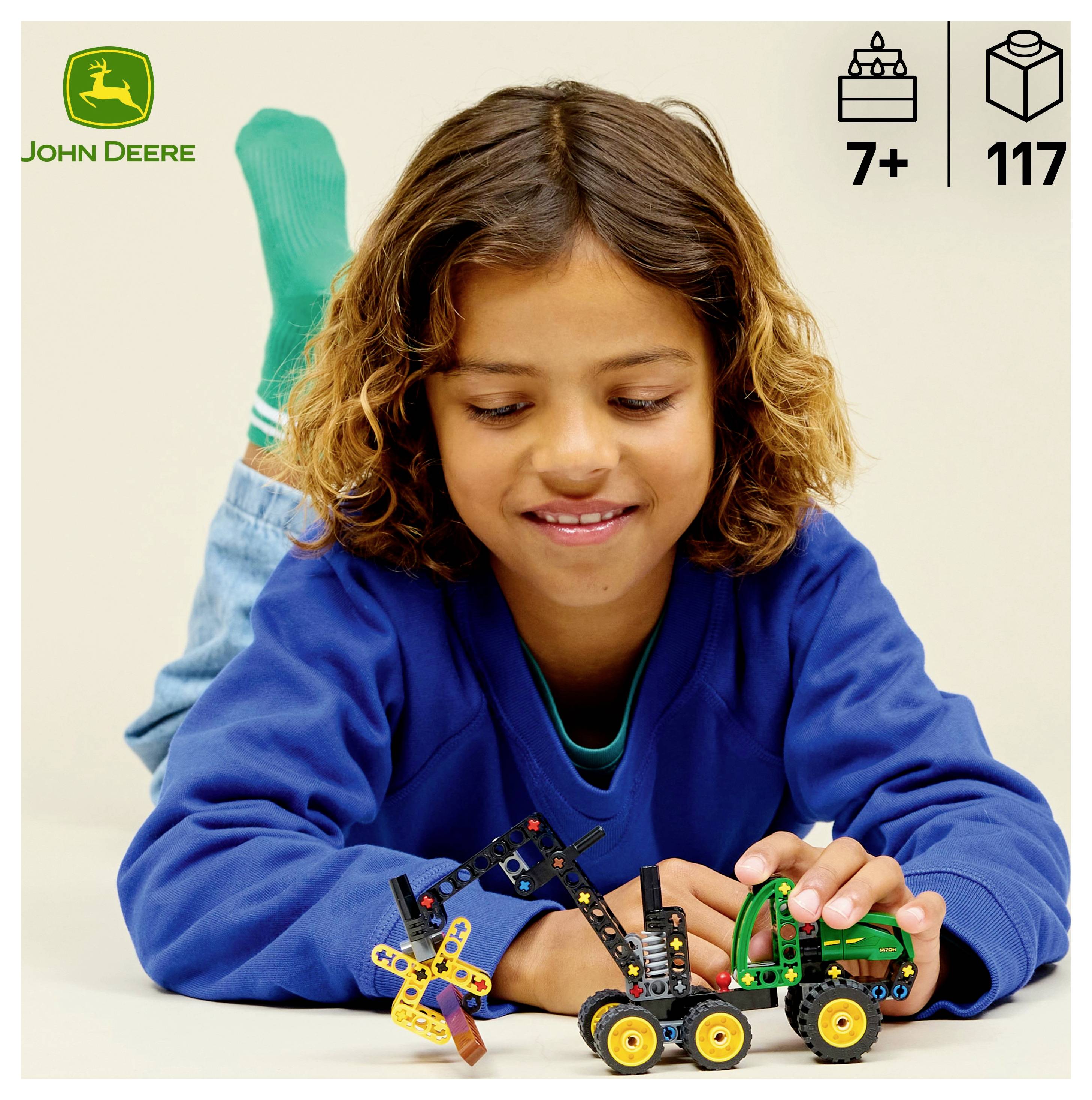 Dieťa v modrom svetri sa hrá s hračkou traktora značky John Deere. Ikony naznačujú, že je vhodná pre deti od 7 rokov a obsahuje 117 dielov.