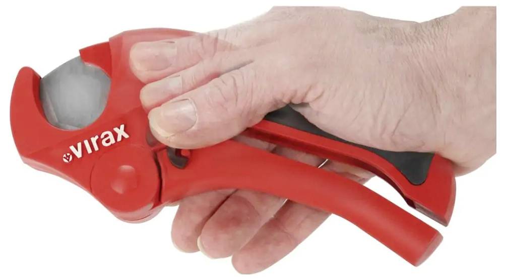 Ruka používajúca červený rezák trubiek Virax na rezanie sivej trubice