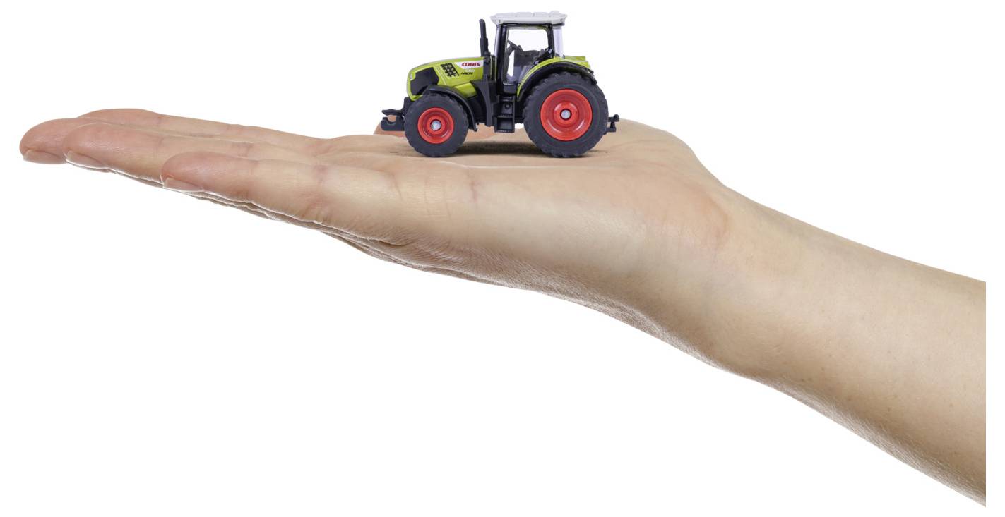 Malý hračkársky traktor s červenými kolesami a zeleným telom spočíva na natiahnutej ruke osoby, zobrazujúc zmenšenú poľnohospodársku vozidlo.