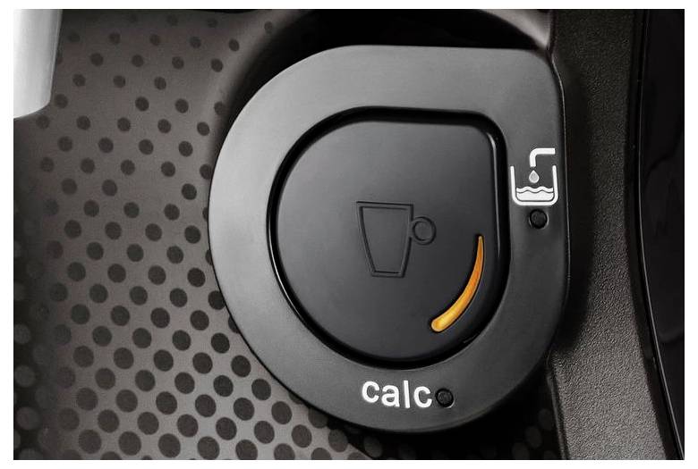 Detailný záber ovládacieho gombíka kávovaru, zobrazujúci oranžový svetelný indikátor s nápisom "calc" nižšie, signalizujúci potrebu odvápnenia.