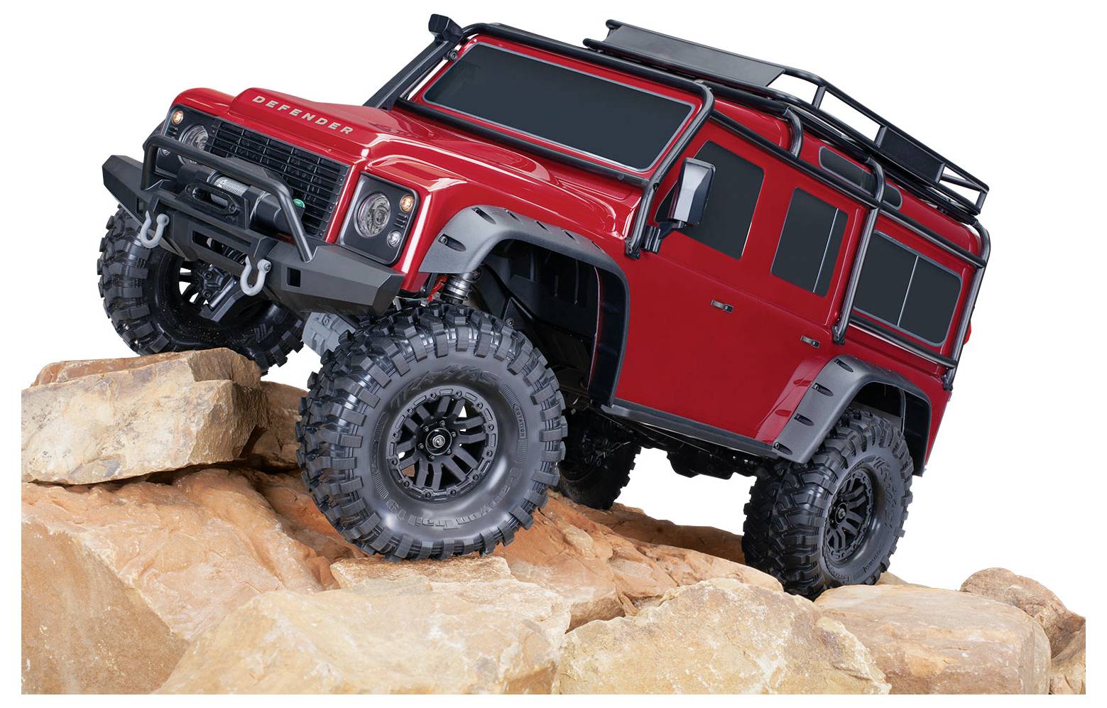 Červený model terénneho vozidla s veľkými pneumatikami je umiestnený na skalistom teréne, pričom ukazuje jeho robustnú konštrukciu a detailné spracovanie.