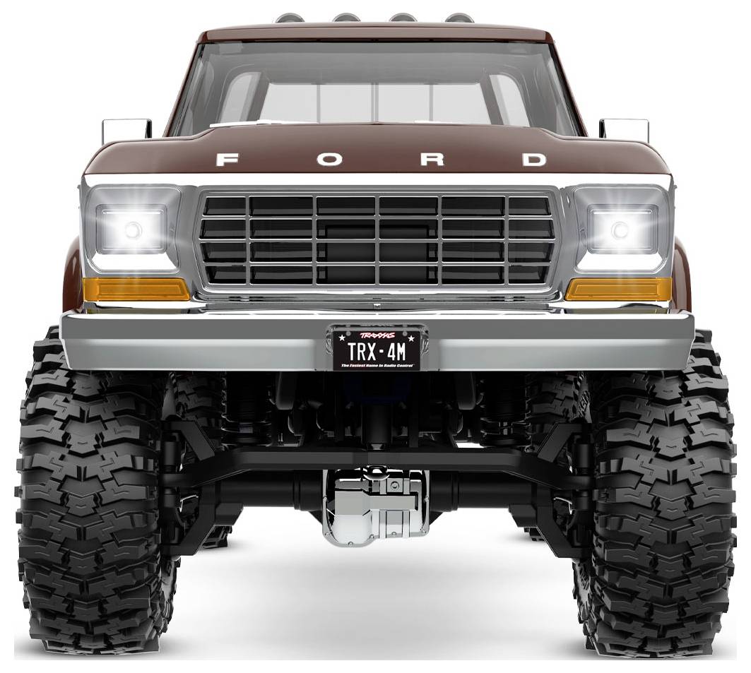 Spredu je zobrazený hnedý Ford pickup s veľkými off-road pneumatikami a prednou poznávacou značkou s nápisom 'TRX-4M'.