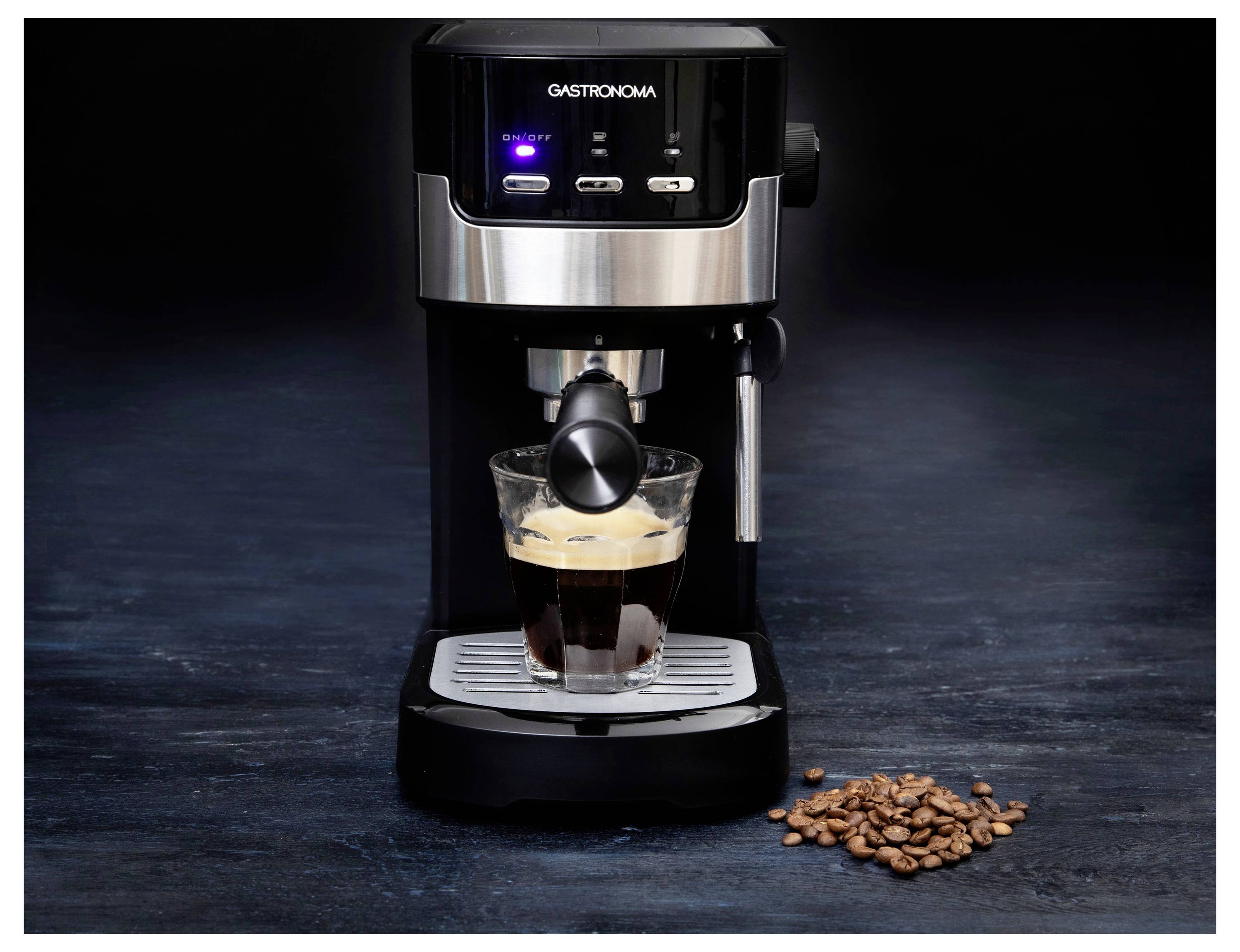 Espresso kávovar varí kávu do priehľadného skleneného šálku s kávovými zrnami roztrúsenými na tmavom povrchu.