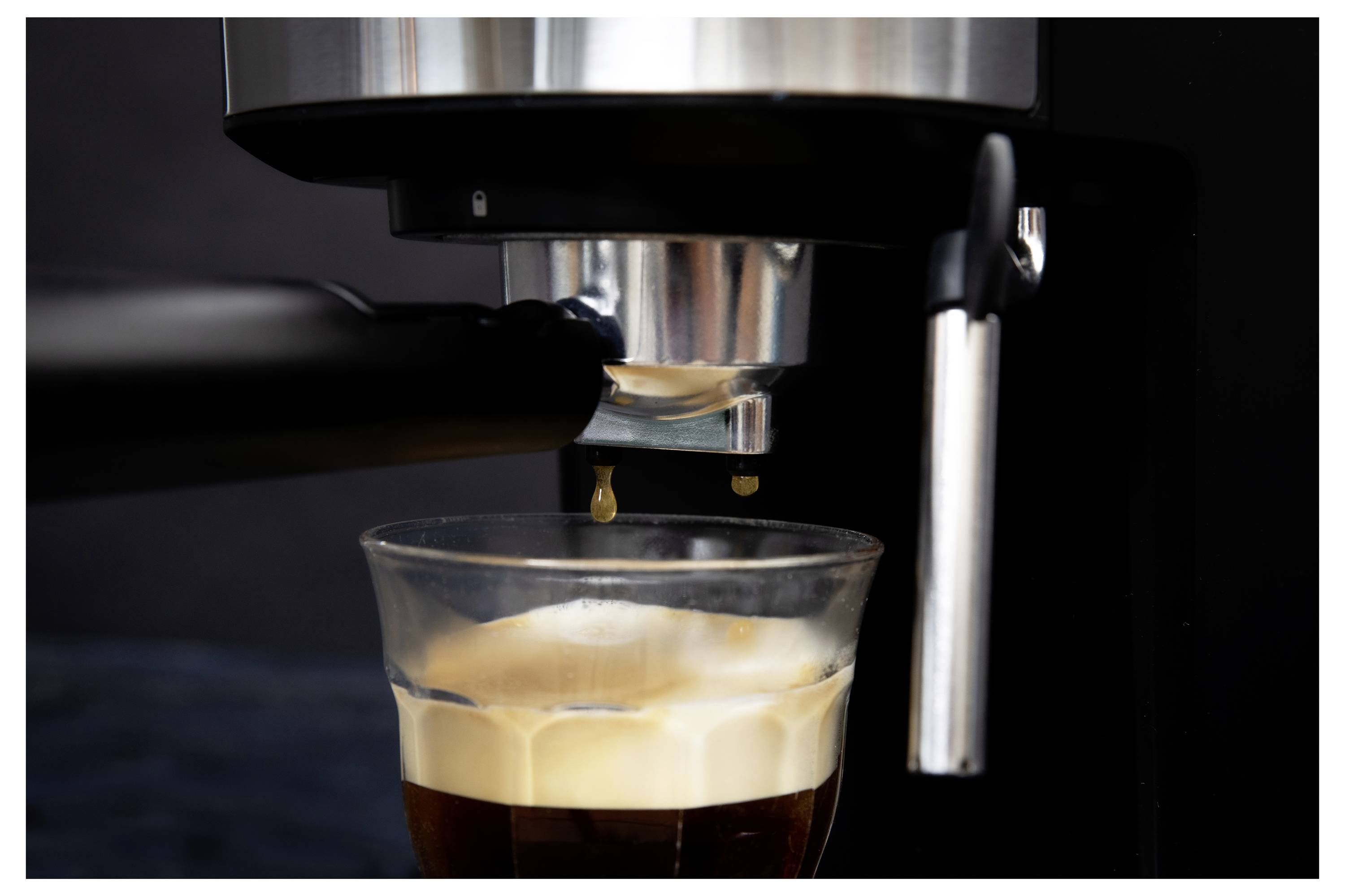 Espresso kávovar, z ktorého sa leje shot do priesvitného pohára, s krémovou vrstvou na povrchu.