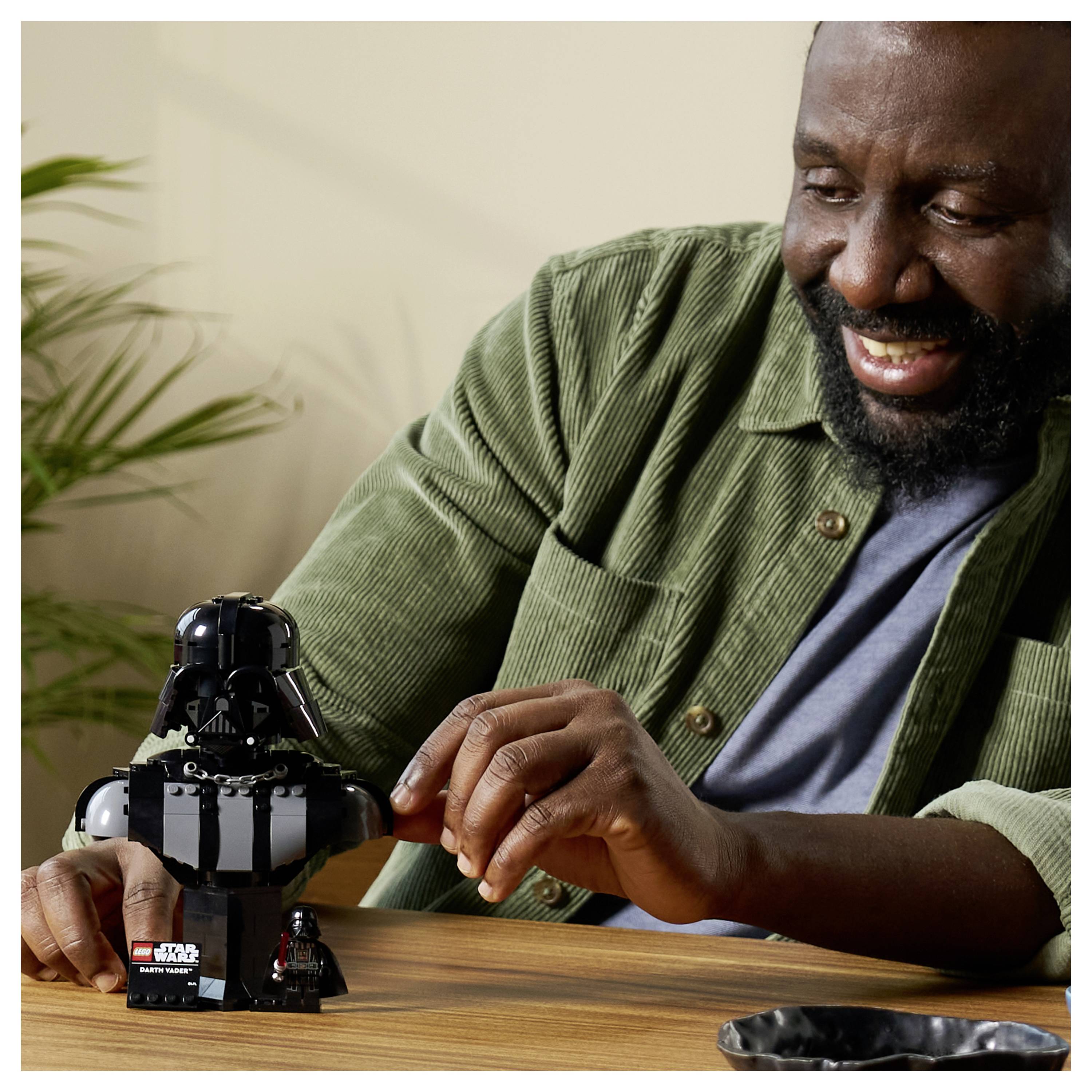 Osoba s úsmevom, ktorá skladá sadu 'LEGO Star Wars', s malou figúrkou Dartha Vadera na stole.