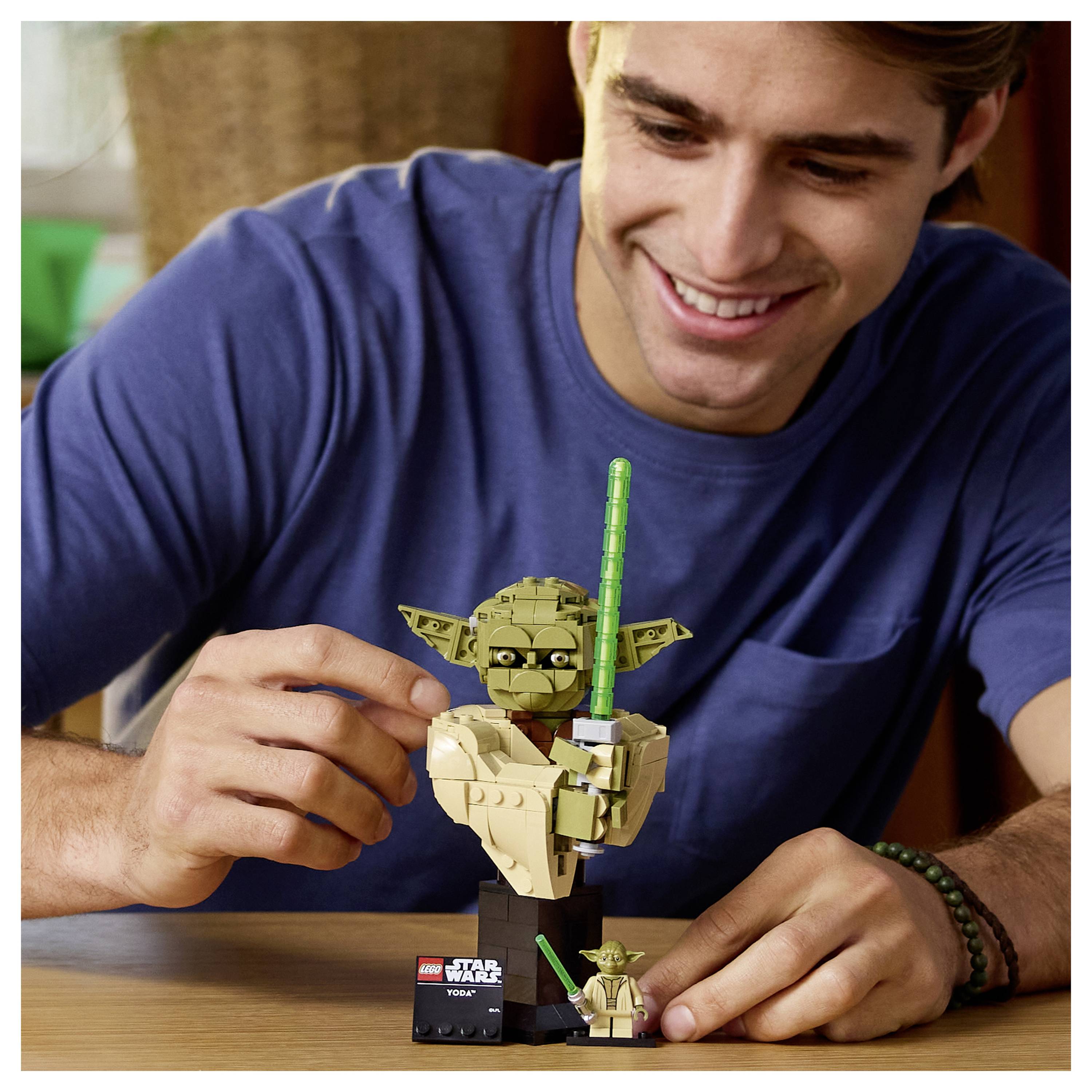 Osoba s úsmevom skladá sadu LEGO Star Wars Yoda na stole, v ruke drží kúsok, vedľa neho je umiestnená malá figúrka.