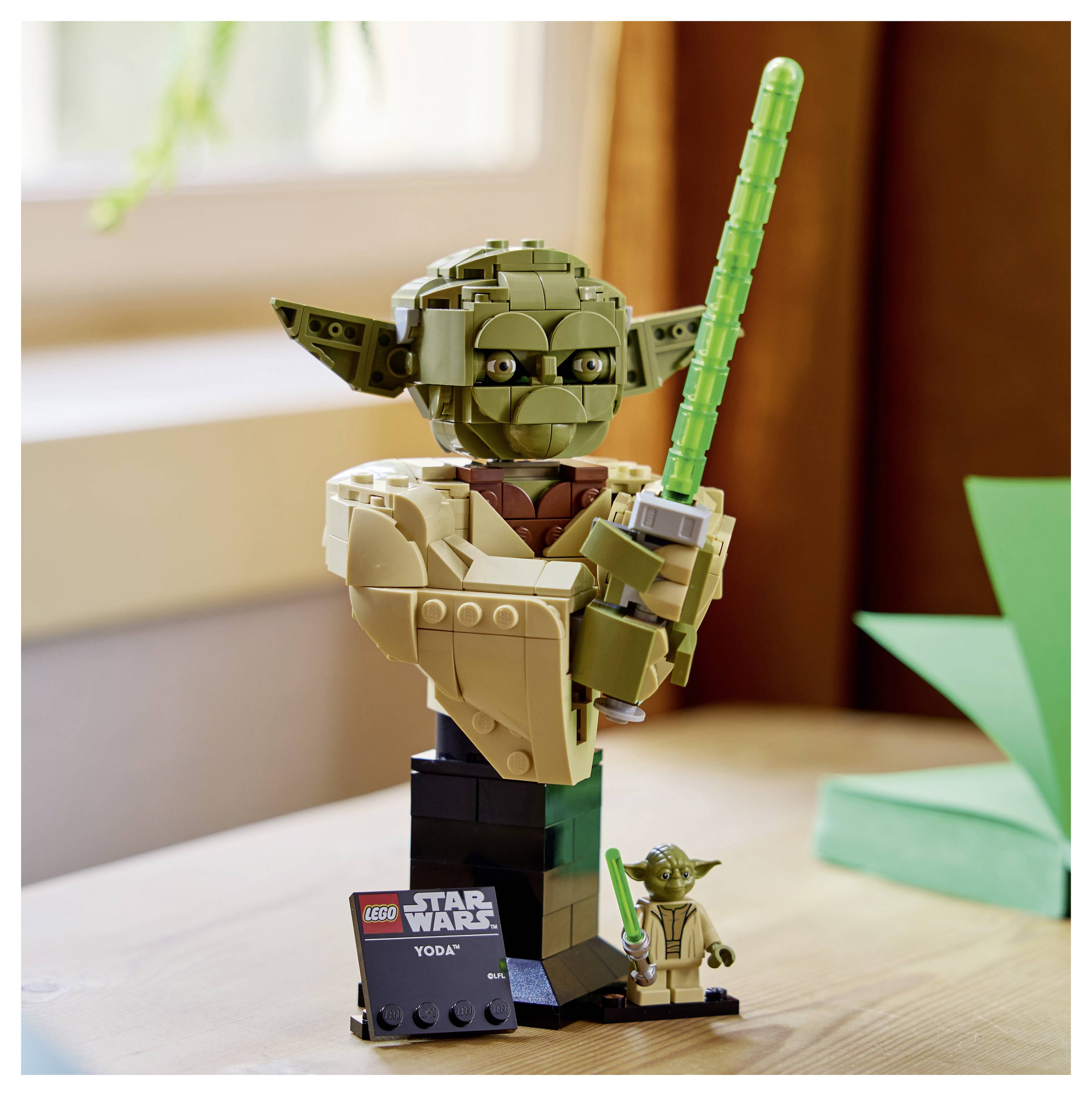 LEGO model Yodyho držiaceho zelený svetelný meč s malou tabuľkou s nápisom „LEGO Star Wars Yoda" na drevenom povrchu.