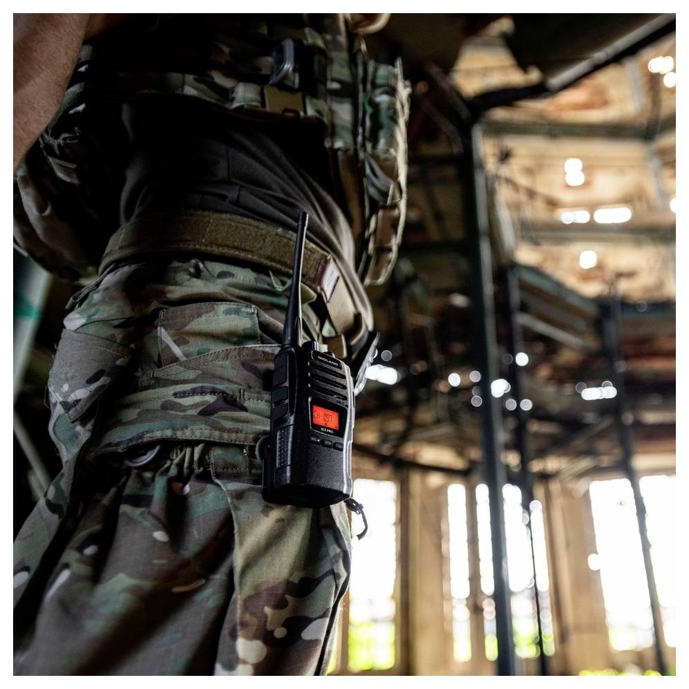 Voják v maskovacím uniforme stojí v zrúcanom budove. Rádiostanica je pripevnená na jeho páse.