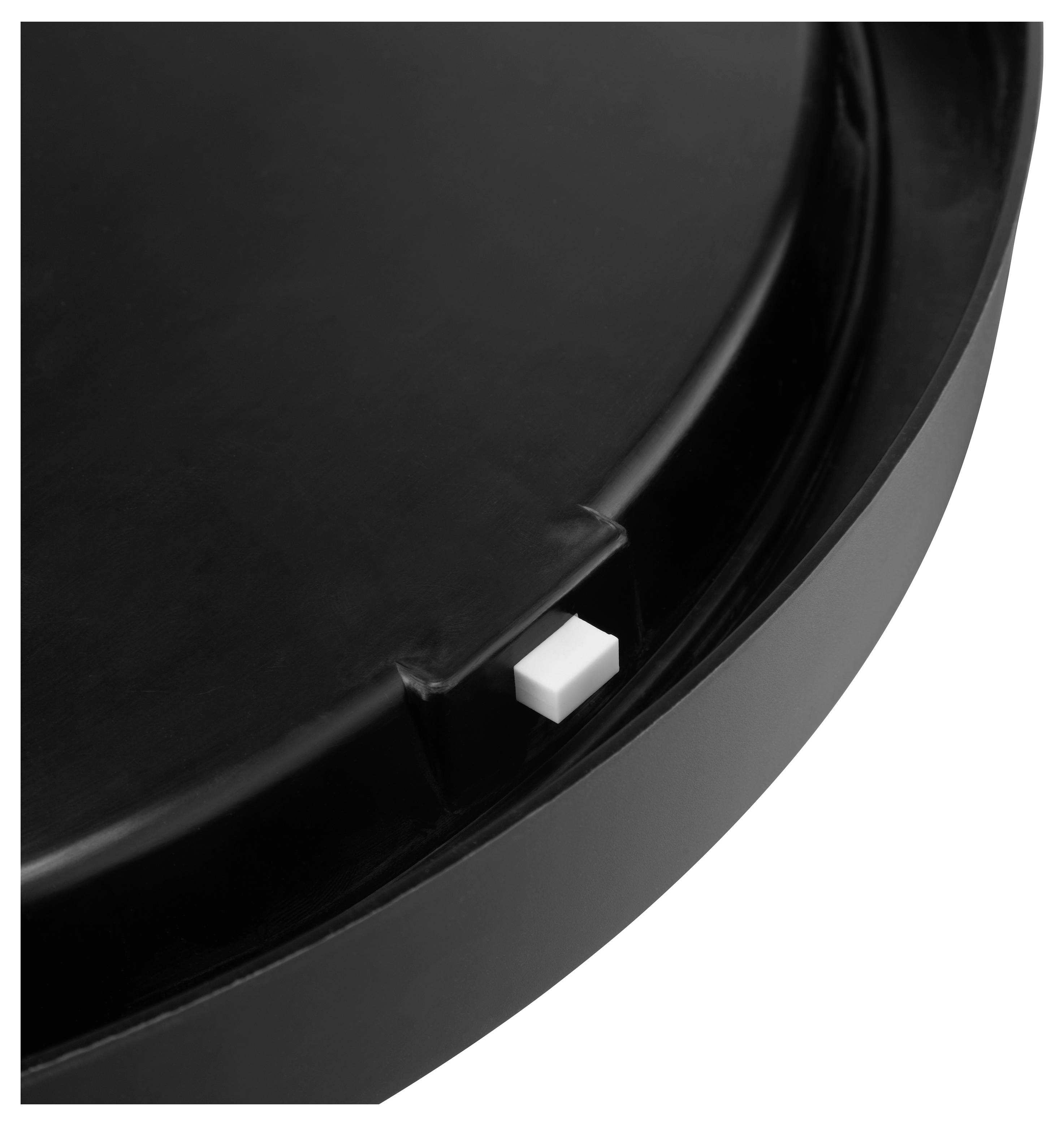 Čierny kruhový predmet s malým bielym štvorcovým tlačidlom vsadeným na boku, pravdepodobne veko alebo kryt so spínačom.