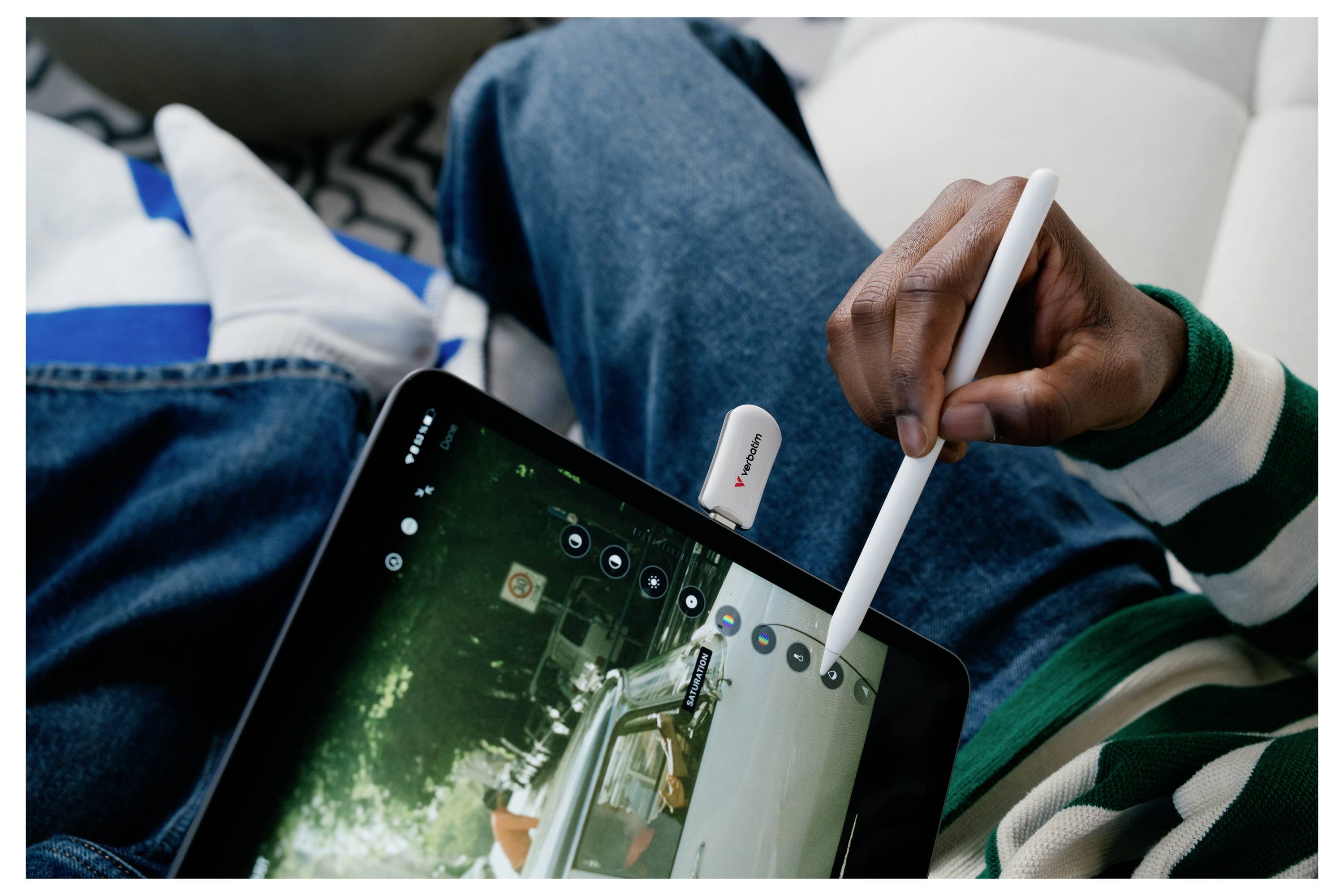 Osoba používajúca biely stylus na tablete, kreslí po obrazovke, pričom sedí na gauči.