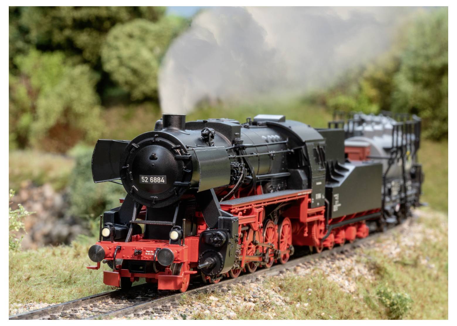 Model parnej lokomotívy s číslom „52 6864" cestuje na miniatúrnej trati cez krásu zelené krajiny so stromami v pozadí.
