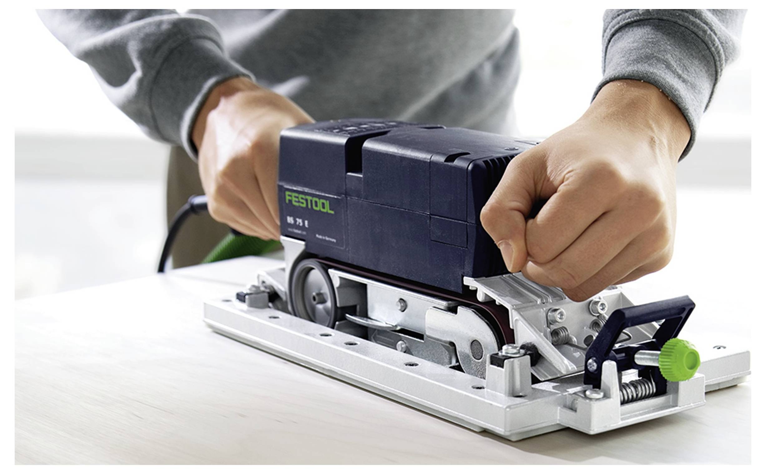 Osoba pracujúca s elektrickým náradím Festool na drevenom povrchu, nastavujúca nastavenia oboma rukami, ilustrujúca použitie náradie a remeselnú prácu.