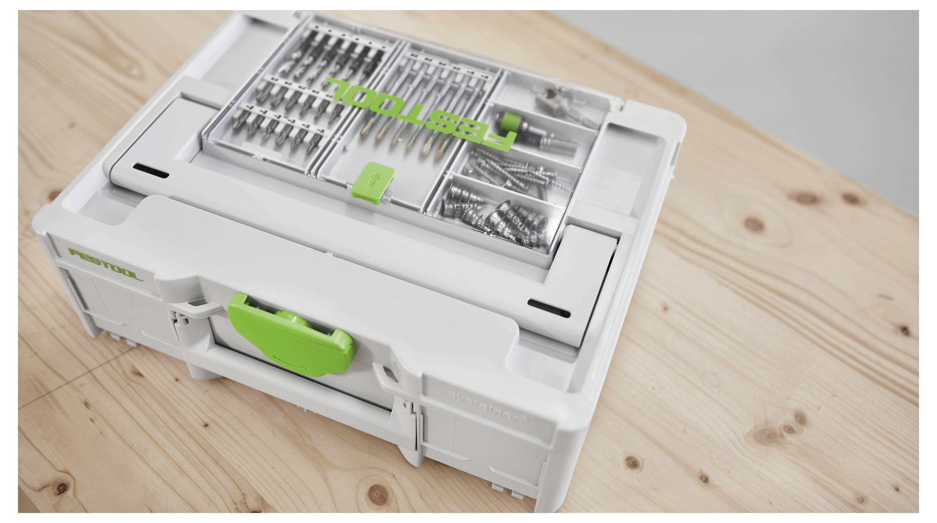 Biela a zelená kufríková skriňa na drevenom povrchu, čiastočne otvorená, aby boli viditeľné usporiadané oddelenia s rôznymi vrtákmi a skrutkami v jej vnútri.