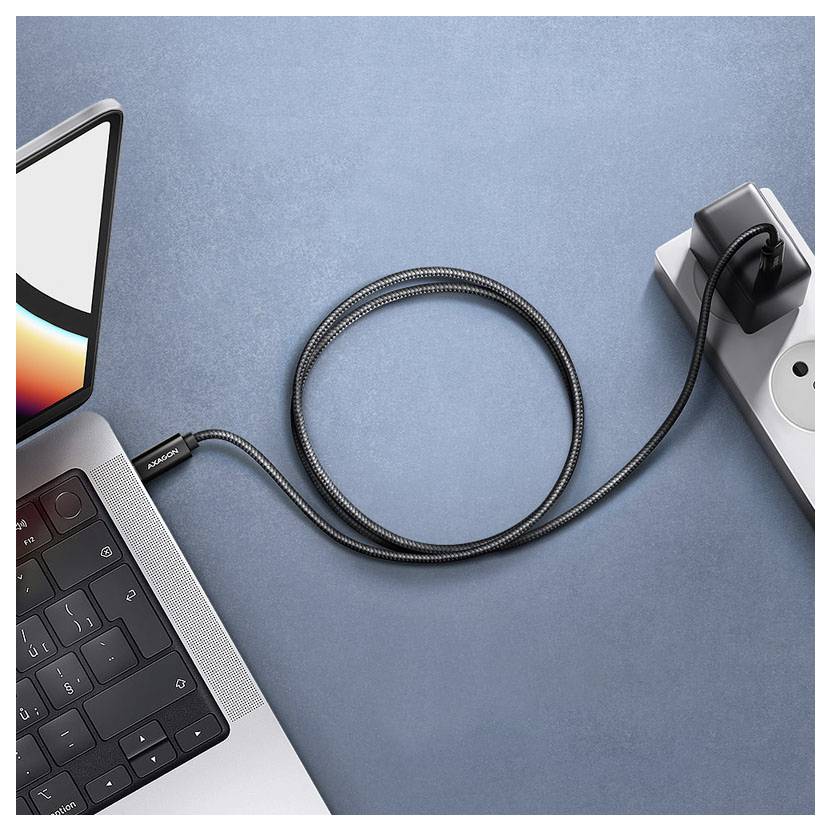 Nabíjací kábel spája notebook s elektrickou zásuvkou prostredníctvom adaptéra na modrom povrchu. Obrazovka notebooku je čiastočne viditeľná.