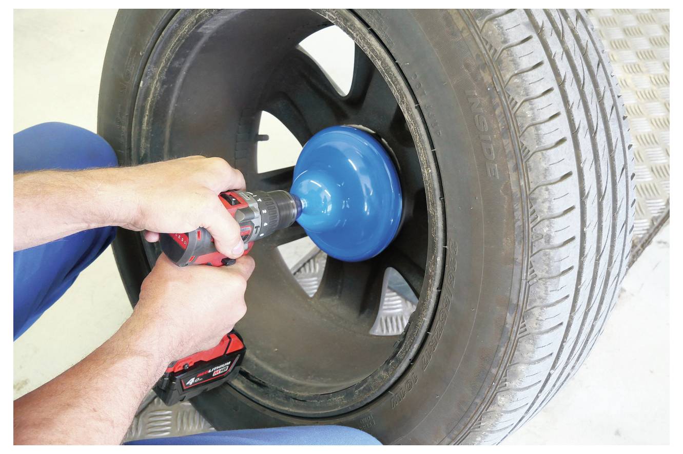 Osoba používa príklepovú vŕtačku na čistenie alebo leštenie ozdobného krytľa kolesa automobilu. Nástroj má na túto úlohu modrý nadstavec.