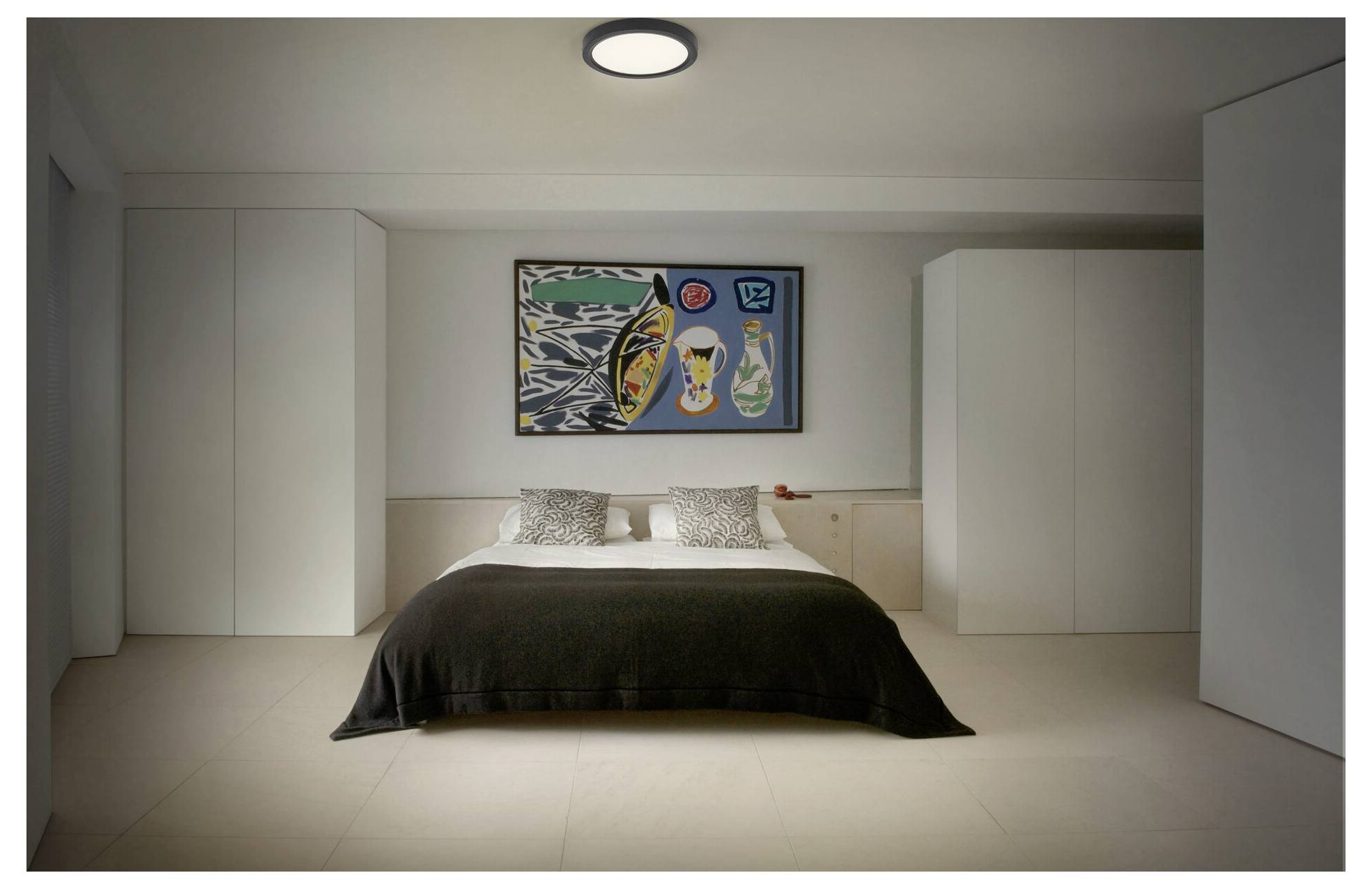 Moderná spálňa s veľkou posteľou, abstraktným umením na stene a bielymi skriňami. Izba má minimalistický dizajn a jemné osvetlenie.