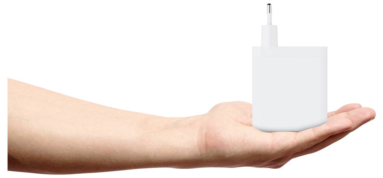 Ruka držiaca bielu USB nabíjačku so zástrčkou na bielom pozadí. Nabíjačka je veľká v porovnaní s rukou.