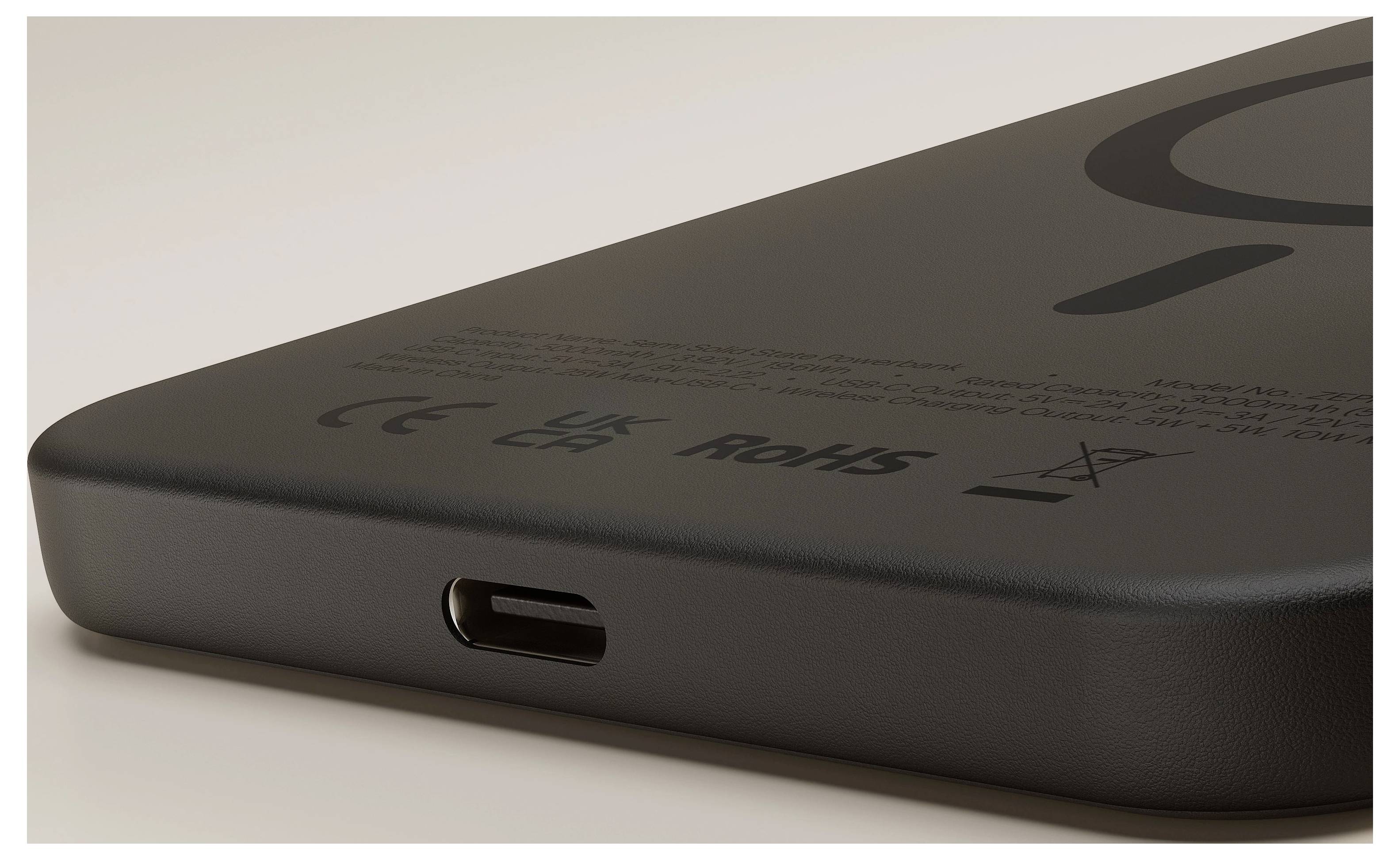 Zblízka zobrazený roh čierneho zariadenia alebo powerbanky, ktorá ukazuje USB-C nabíjací port a značky zhody na zadnej strane.