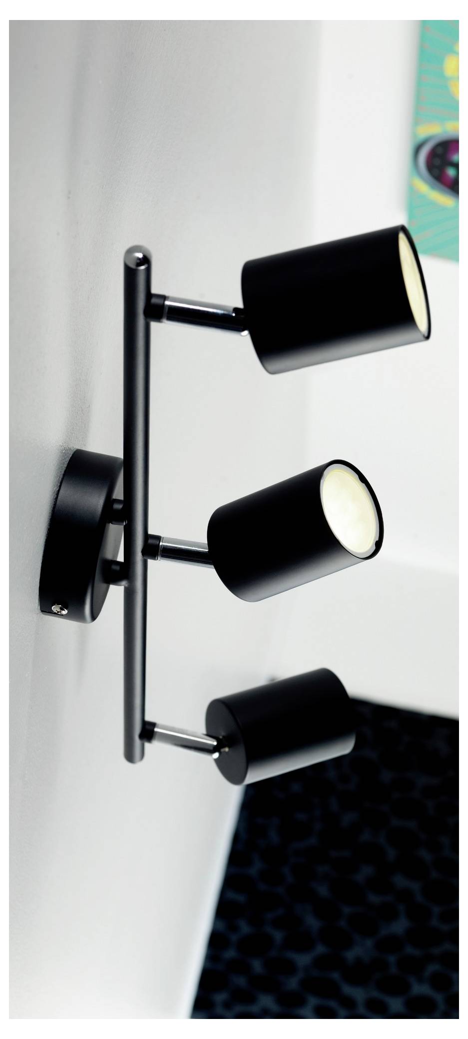 Tri čierne cylindrické reflektory umiestnené na vertikálnom nástennom držiaku, osvetľujúce blízku plochu.