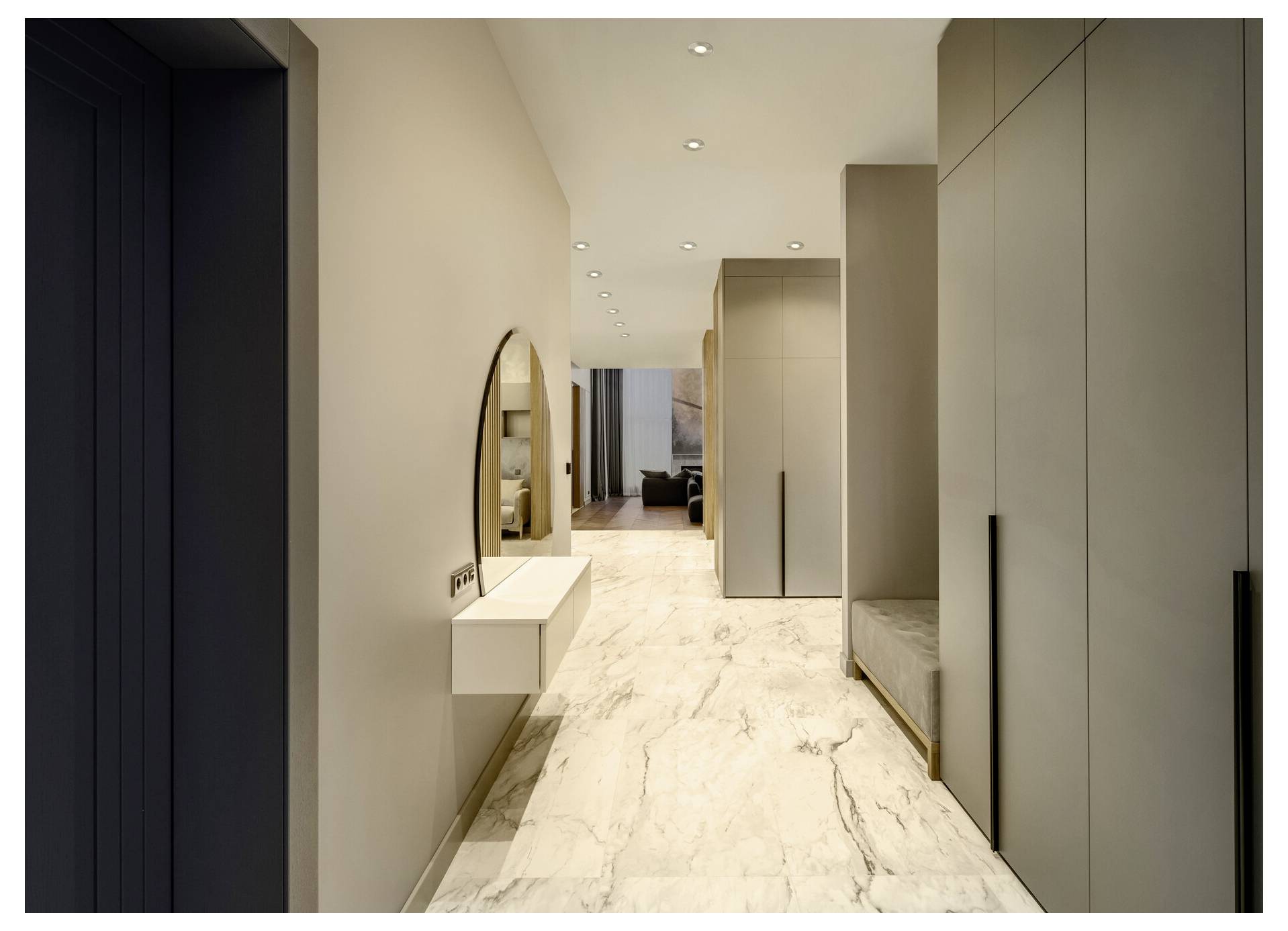 Moderná chodba s mramorovou podlahou, krémovými stenami, okrúhlym zrkadlom a elegantnými, od podlahy po strop siahajúcimi skrinkami na pravej strane.