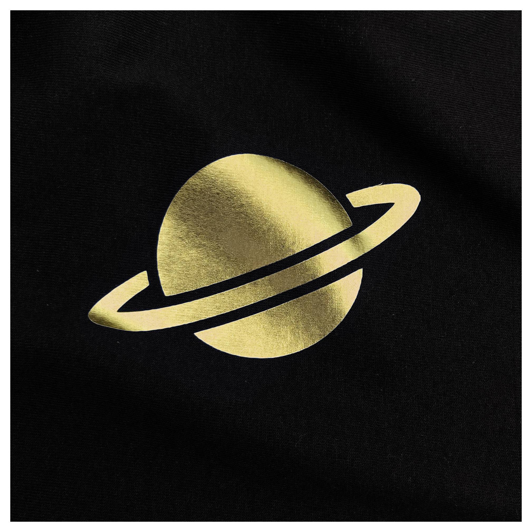 Zlatá silueta planéty s prstencami, ktorá pripomína Saturn, na čiernom pozadí.