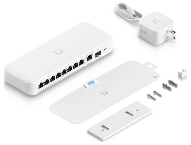 Sieťový prepínač Ubiquiti s viacerými portmi Ethernet, napájací adaptér, montážna konzola, skrutky a príslušenstvo, usporiadané na bielom povrchu.