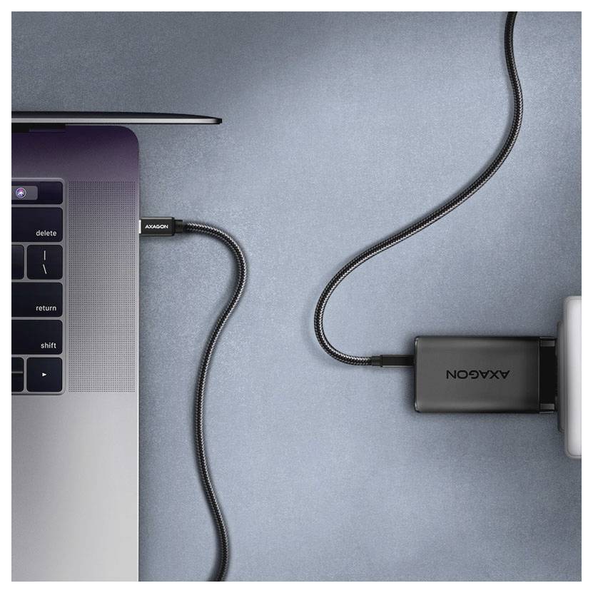 Laptop pripojený kabelom na čierny adaptér Axxagon a externé zariadenie na modrej ploche.