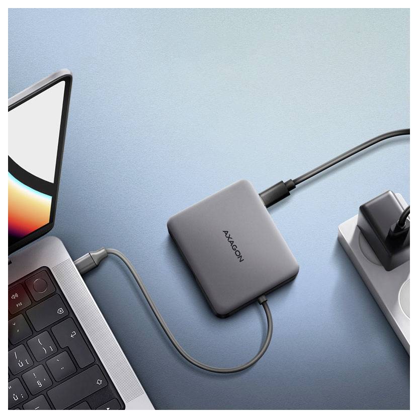 USB-C hub pripojený k notebooku, monitoru a napájaciemu adaptéru na modrom stole.