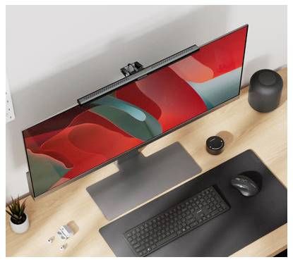 Pohľad z vrchu na minimalistickú kanceláriu s veľkým monitorom zobrazujúcim abstraktnú červenú a tmavozelenú tapetu, klávesnicu, myš, reproduktor a malé doplnky.