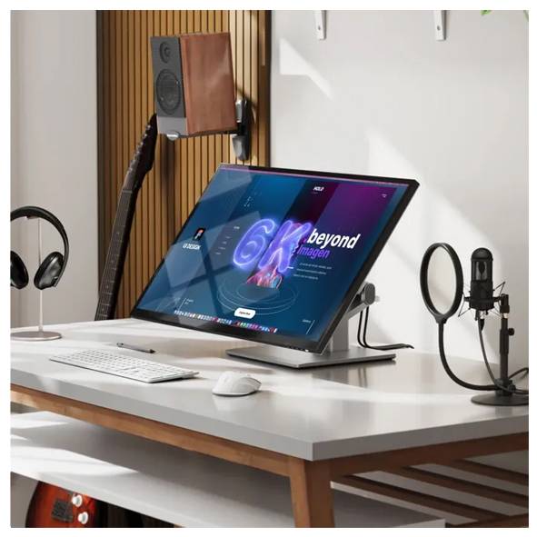 Moderná pracovná stanica so sklopeným monitorom zobrazujúcim "6K beyond", klávesnica, myš, slúchadlá, gitara, reproduktory a mikrofón na bielom stole.