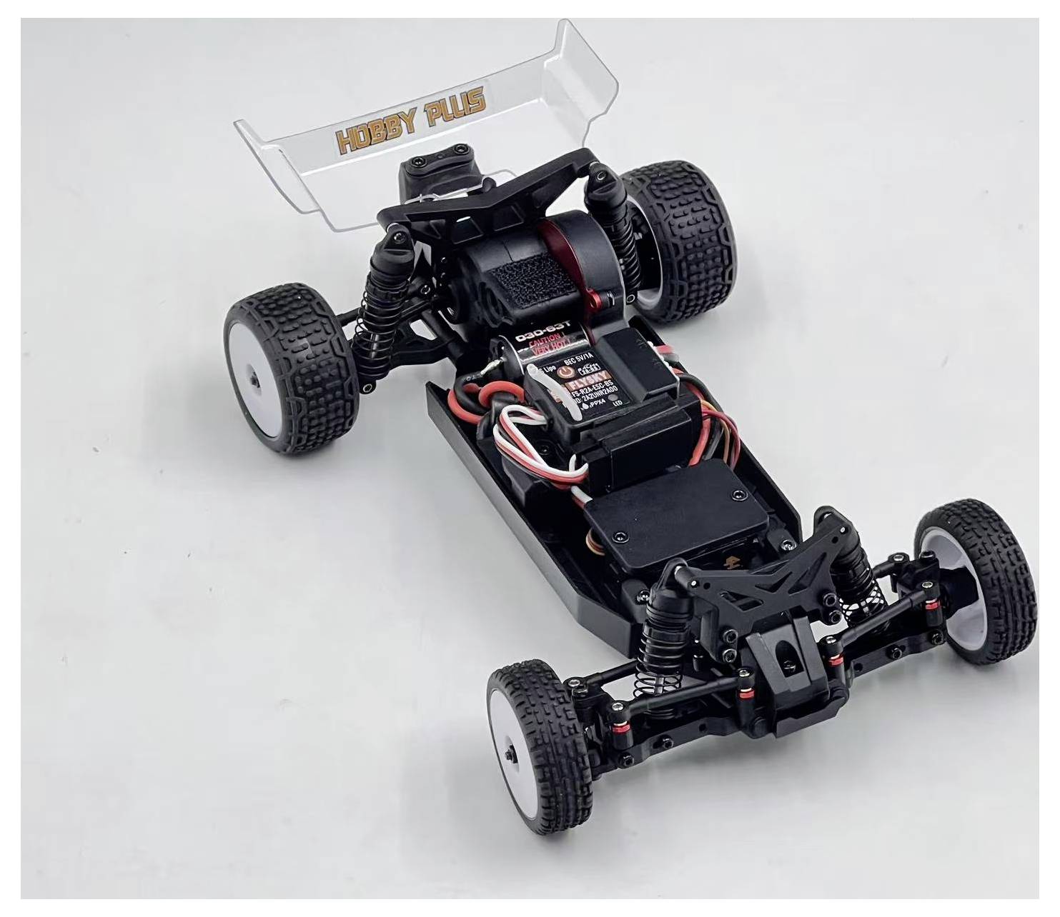 Rozložená RC buggy podvozka s odhalenou batériou, motorom, zavesením a štyrmi kolesami na jednoduchom bielom pozadí.