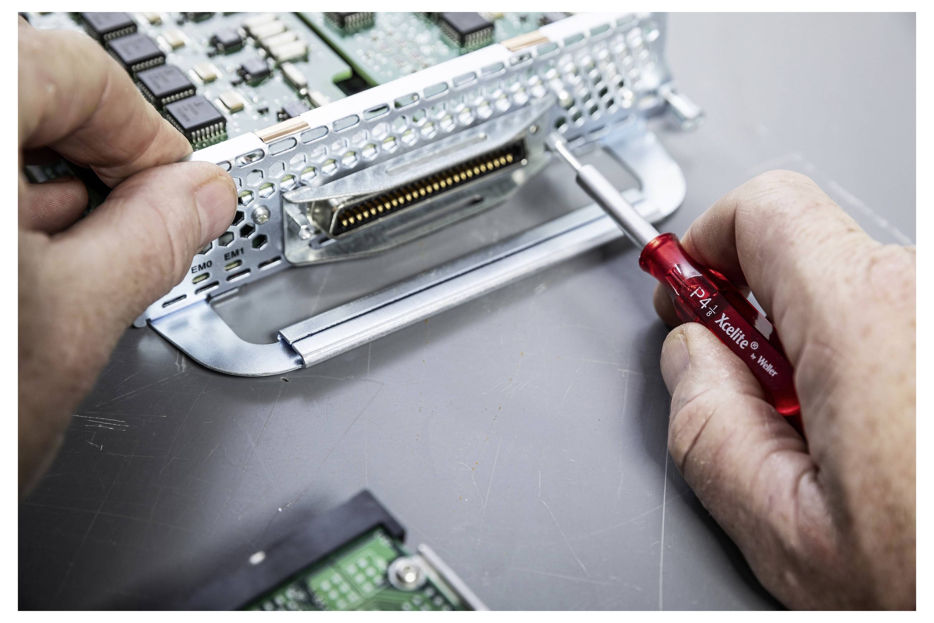 Ruky používajú malý skrutkovač na nastavenie kovového elektronického komponentu alebo konektora vo vnútri zariadenia na pracovnom stole.