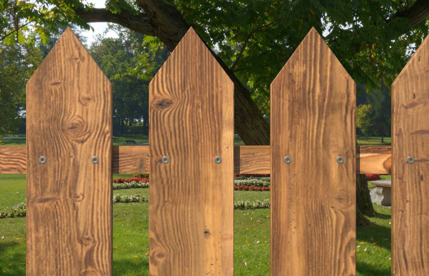 Drevené oplotenie s palisádami v popredí, za ním viditeľný park a veľký strom.