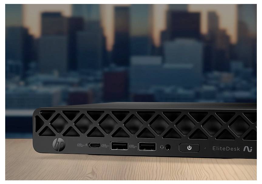 Predný pohľad na HP EliteDesk mini stolný počítač s tlačidlom napájania a USB portami na stole, s rozmazaným mestským horizontom v pozadí.
