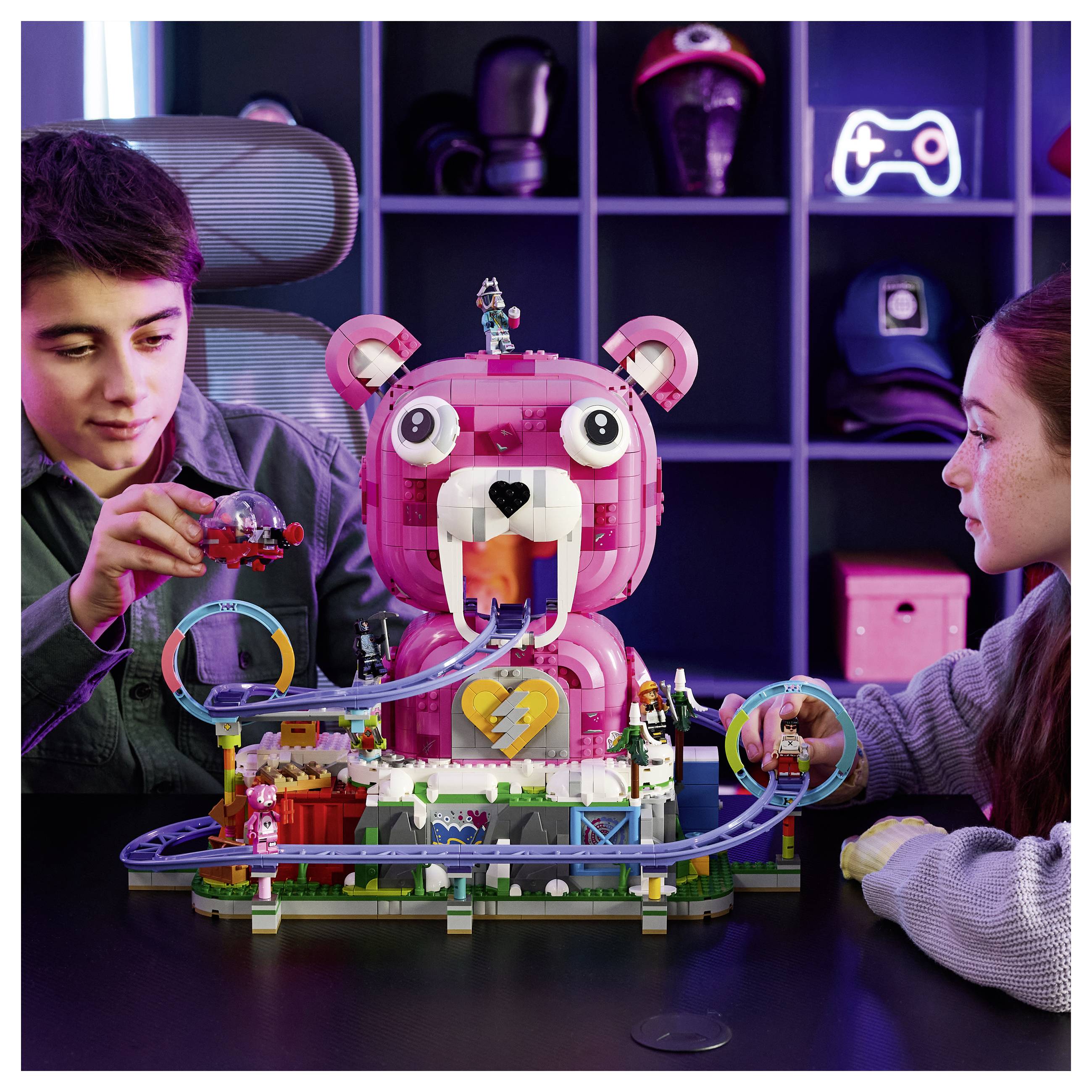 Dvaja chlapci hrajú si s ružovým LEGO horským vlakom s motívom medveďa na stole, v centre je veľký model medveďa a koľaj sa točí okolo neho.