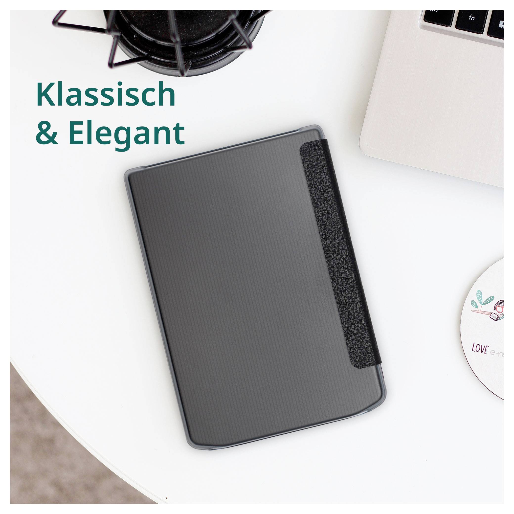 Sivé štruktúrované puzdro na tablet na bielom stole vedľa notebooku, s nemeckým textom „Klassisch & Elegant" zdôrazňujúcim klasický, elegantn štýl.