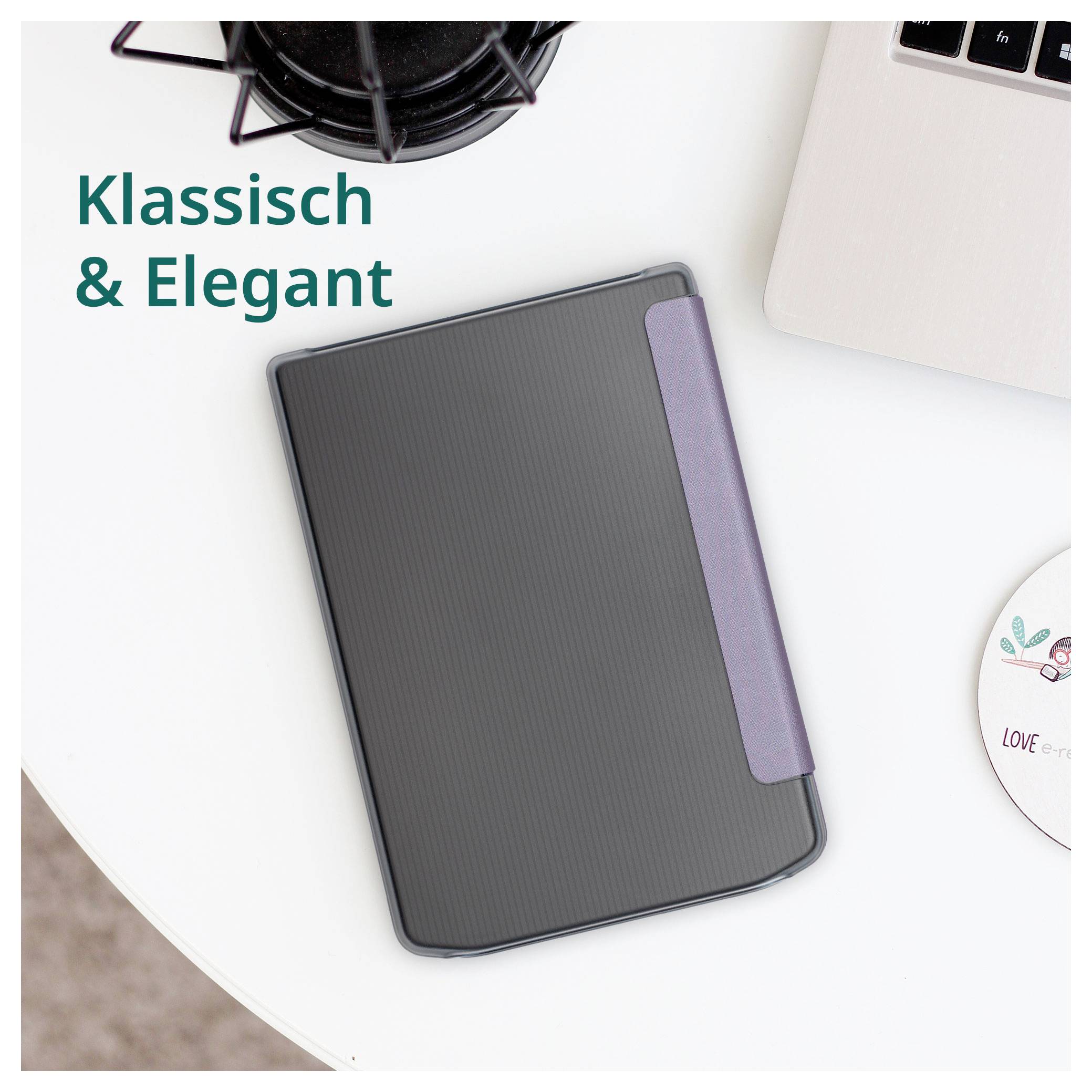 Čierny vrúbkovaný zápisník alebo plánovač s fialovým elastickým pásom, zobrazený na bielom stole vedľa notebooku a šálky kávy s textom "Klassisch & Elegant".