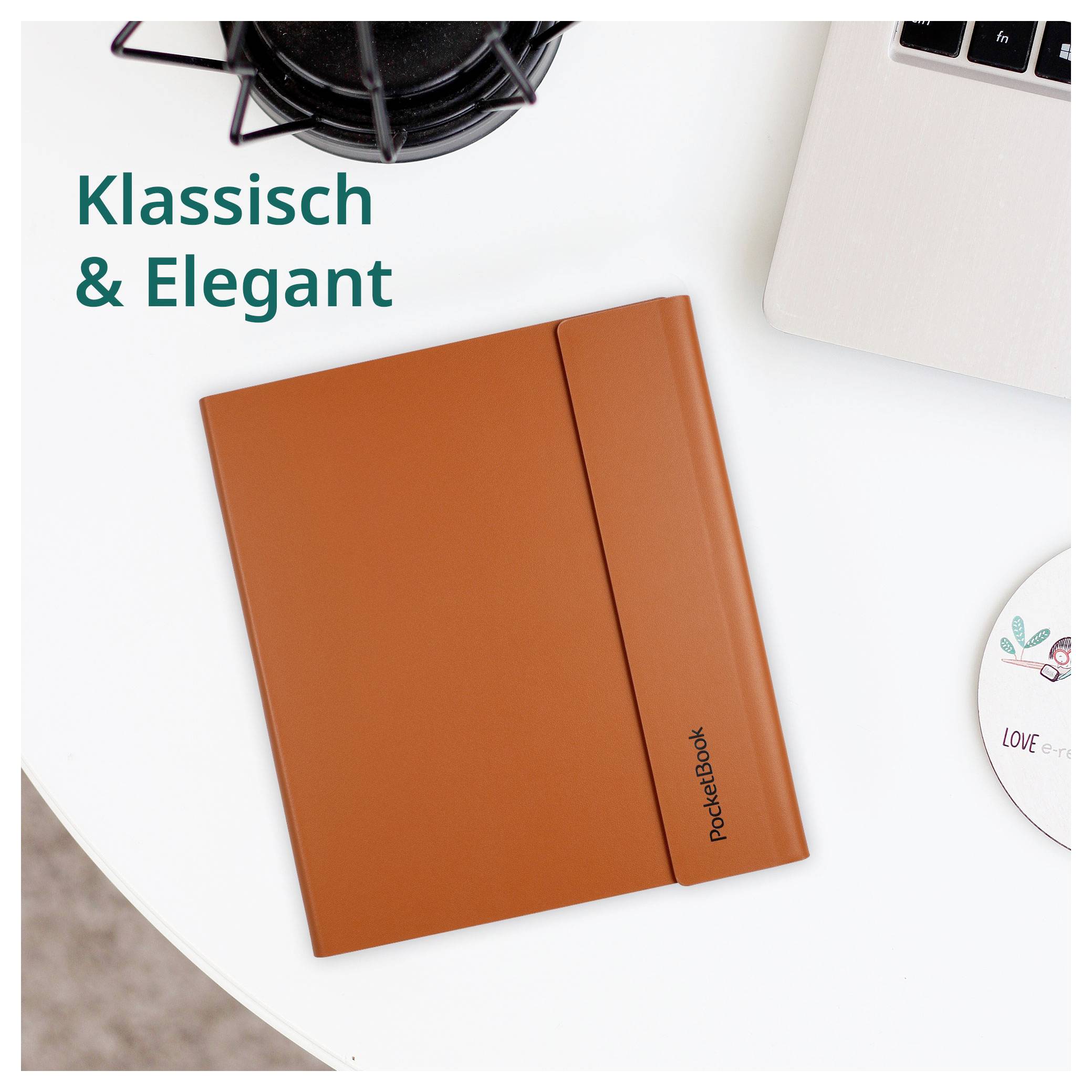Oranžový notebook PocketBook na bielom stole s notebookom a šálkou kávou; text hovorí "Klassisch & Elegant" a "PocketBook"