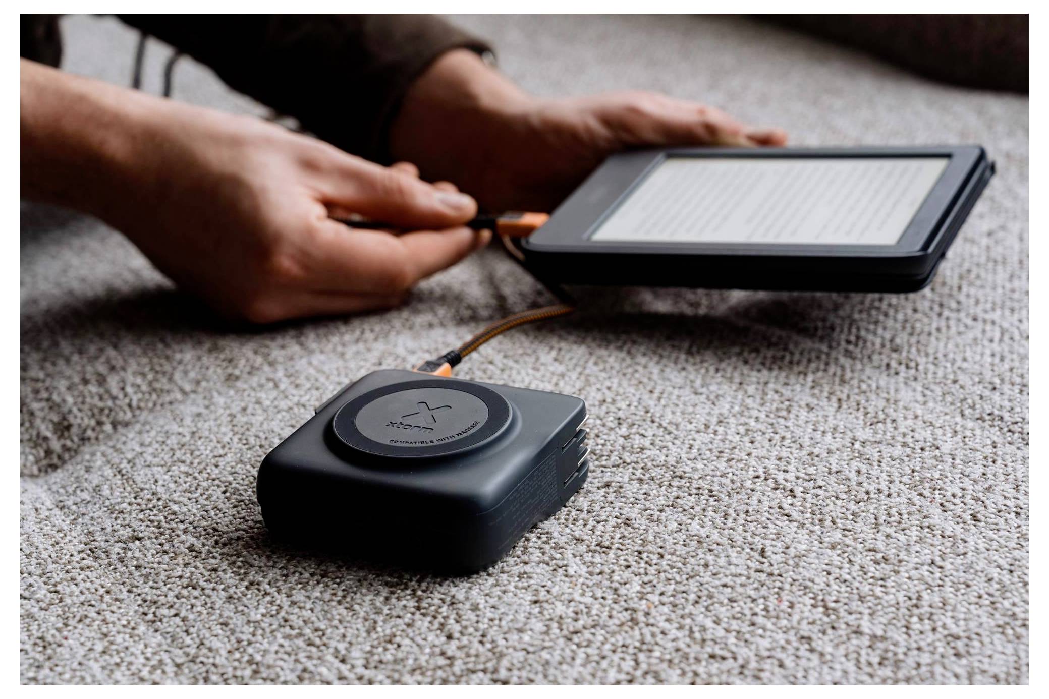 Osoba nabíja elektrickú čítačku pomocou prenosnej powerbankuky cez kábel na kobercovej podlahe.