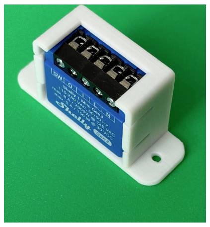 Malý modrý elektrónický modul v bielej plastovej konzole so skrutkovacími svorkami, zobrazený na zeleného pozadí.
