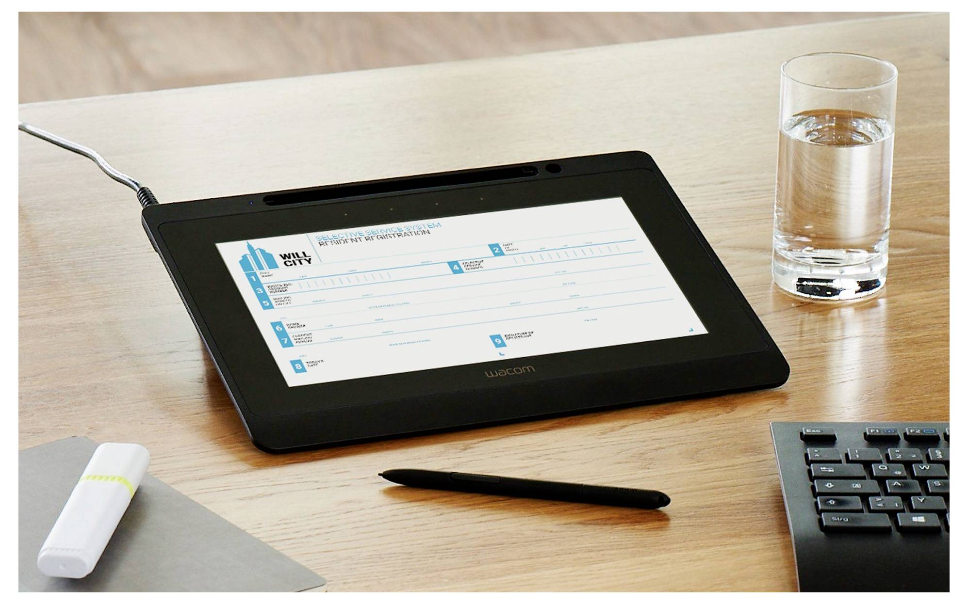 Tablet na stole zobrazujúci webový formulár, vedľa ktorého sú pero, klávesnica, pohár vody a USB kľúč.