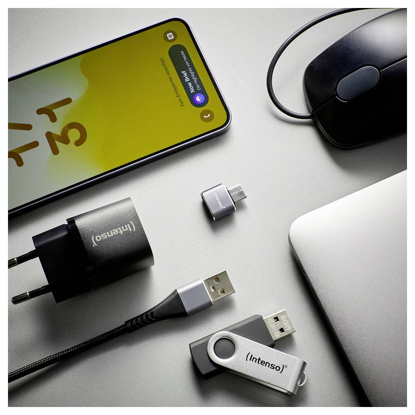 Smartphone pripojený k niekoľkým USB adaptérom a káblom vedľa myši a notebooku, ilustrujúci nabíjanie zariadení a konektivitu.
