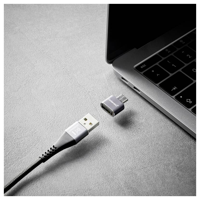 Kábel USB a malý adaptér sa vznášajú v blízkosti portu USB-C notebooku, čo naznačuje pripojovací alebo konverzný prístroj.