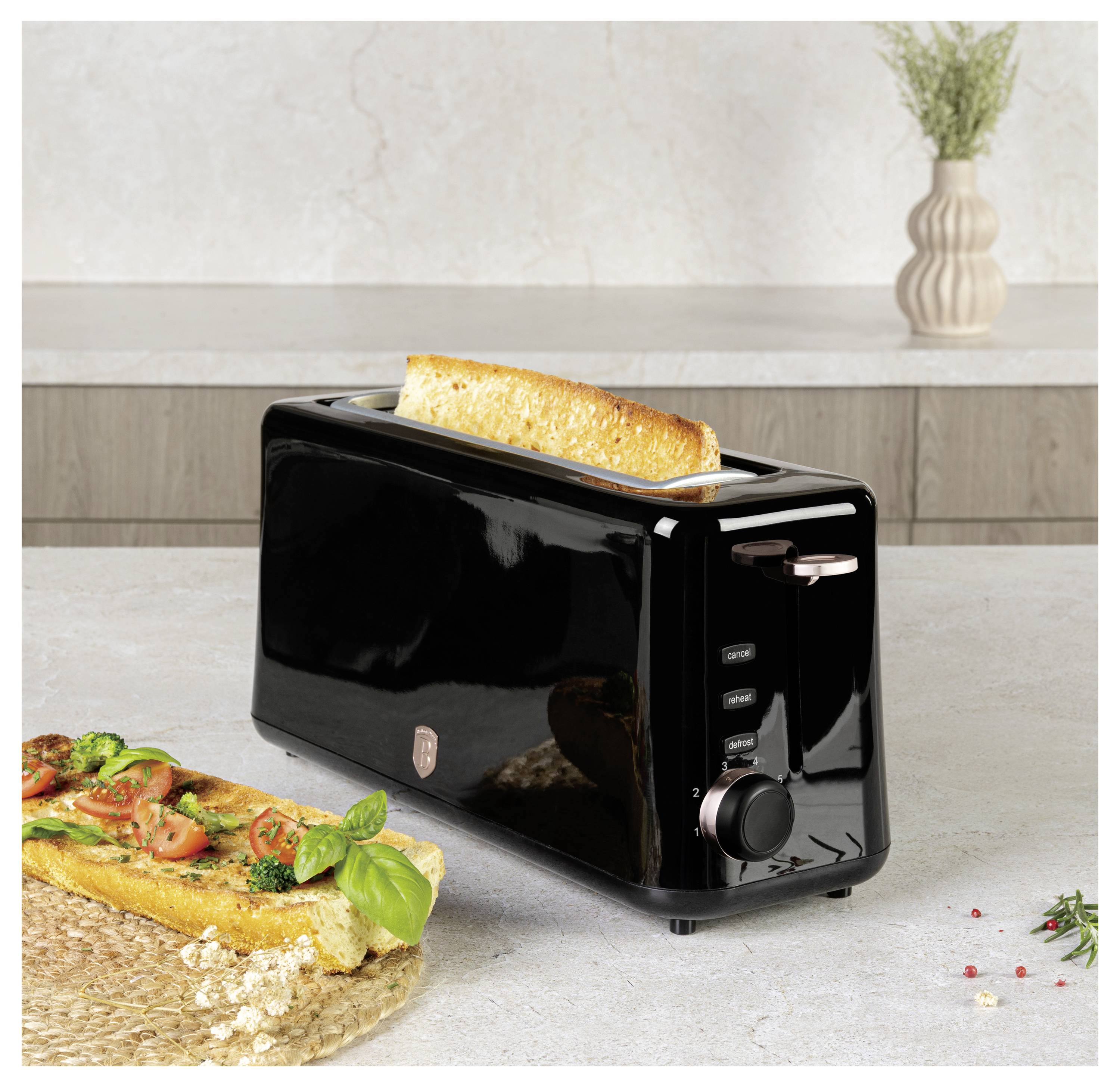 Čierny hriankovač s jedným kúskom chleba, ktorý sa pražuje, vedľa nakrájaného bazalkovo-paradajkového toastu na kuchynskom pulte.